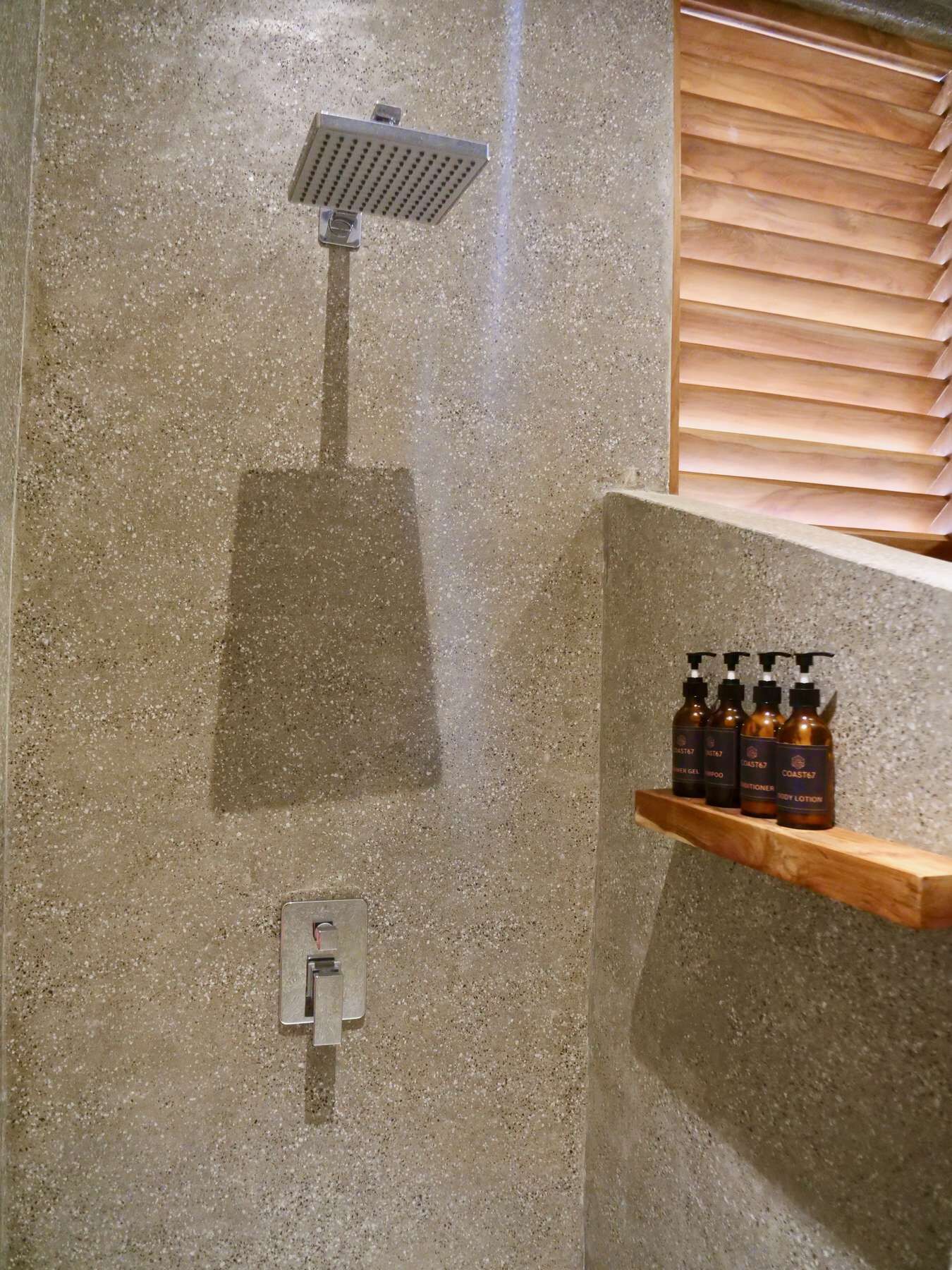 A shower with a handheld showerhead, a control panel, and a wooden shelf with bottles.