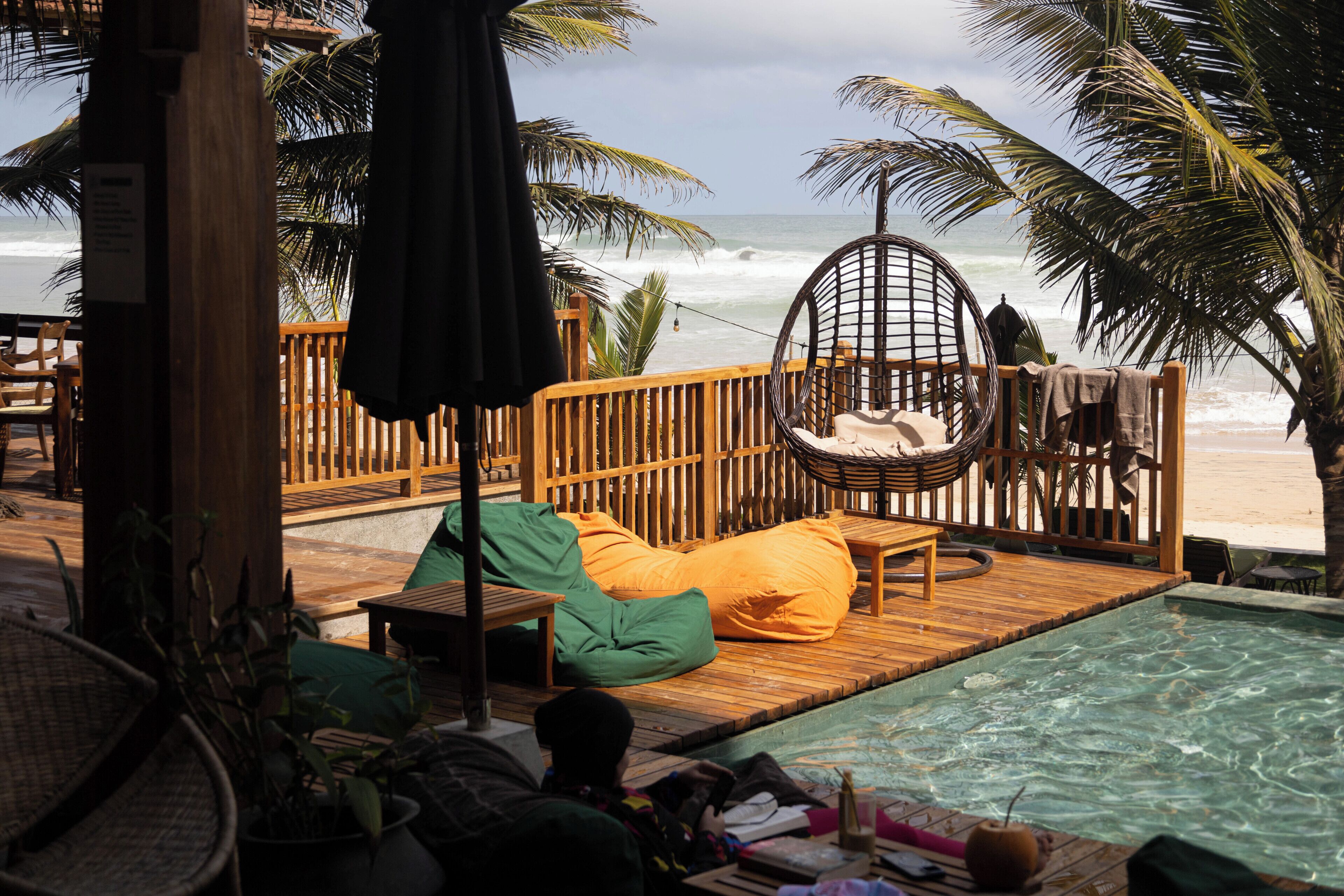 A wooden deck with a pool, a hanging chair, and a lounge chair with a cushion.