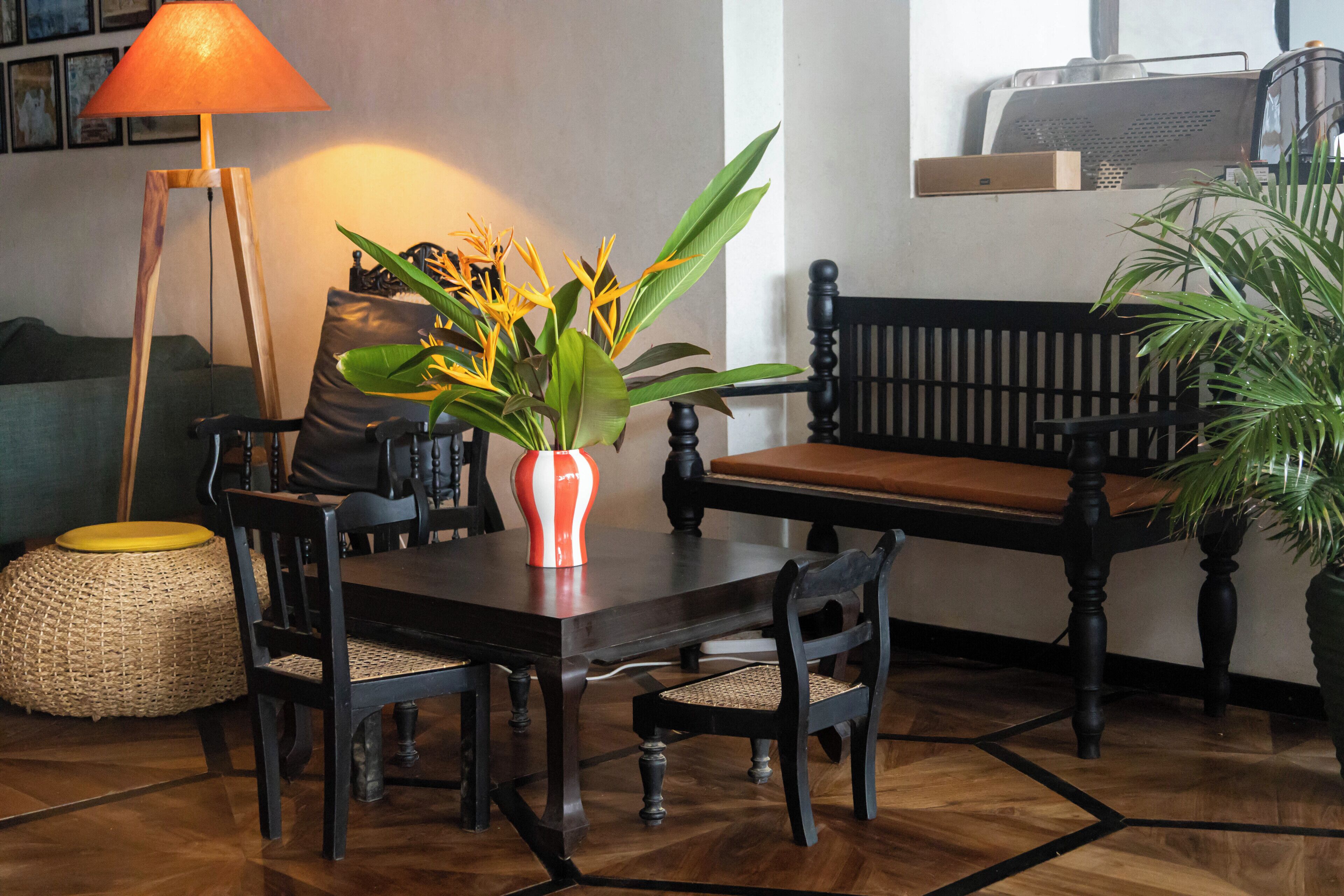 A dining area with a wooden table, chairs, a bench, a vase with flowers, a lamp, and a potted plant.