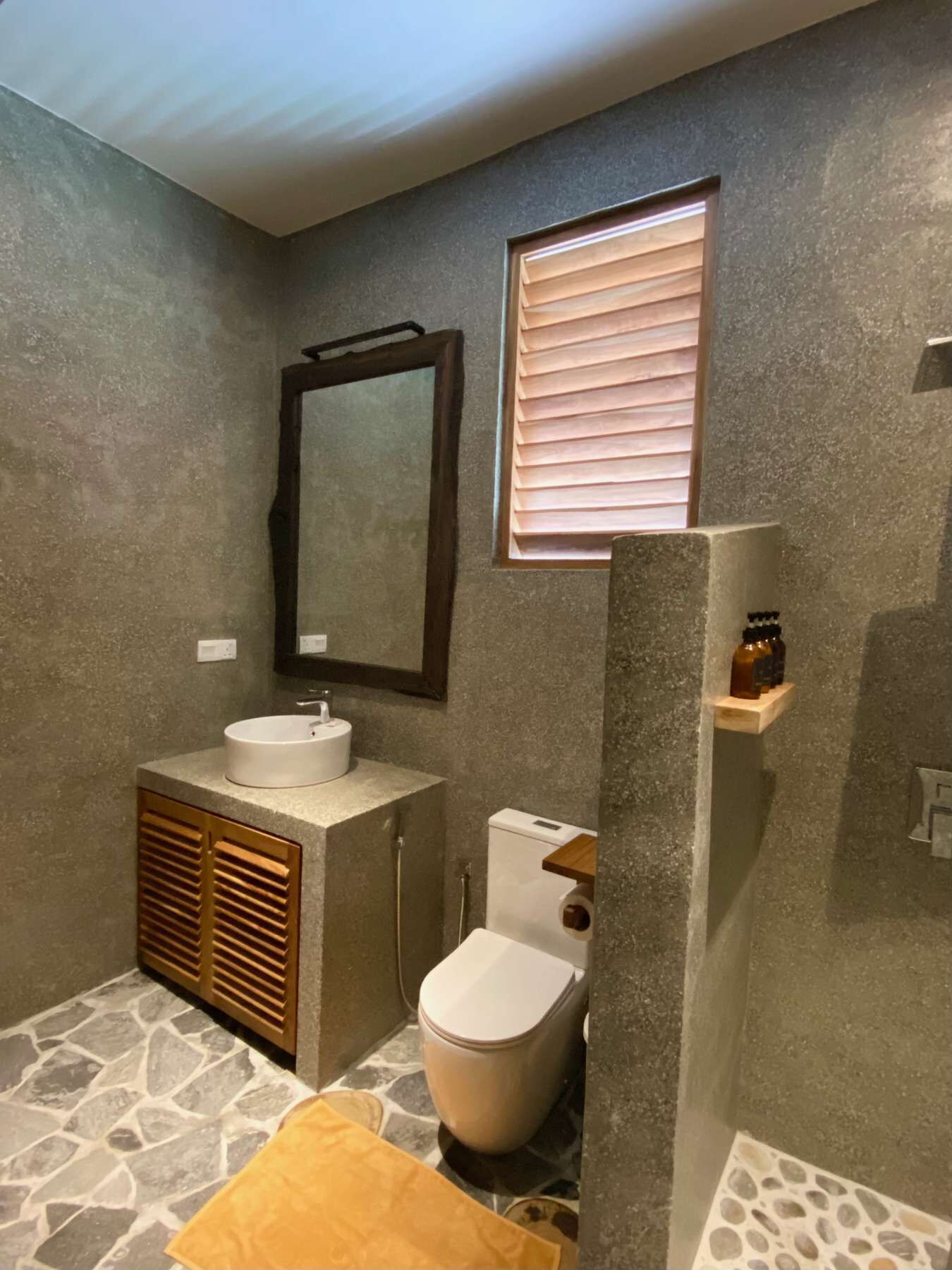 Un bagno con pavimento in pietra, lavandino bianco, water e specchio.