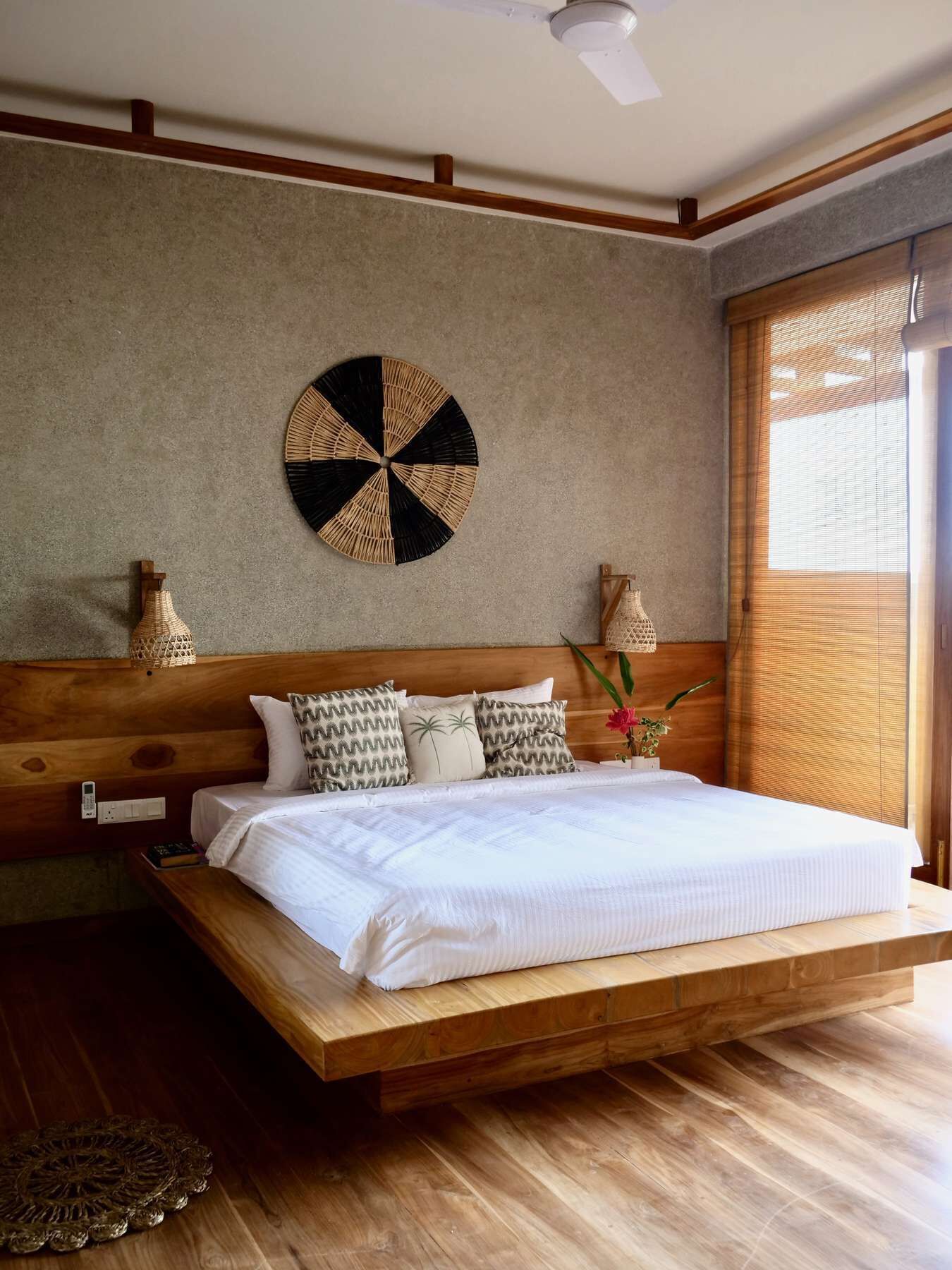 Une chambre avec un lit en bois, un élément de décoration circulaire au mur et une fenêtre avec des stores.