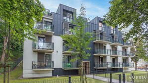 A modern apartment complex with multiple balconies, a fenced courtyard, and surrounding greenery.
