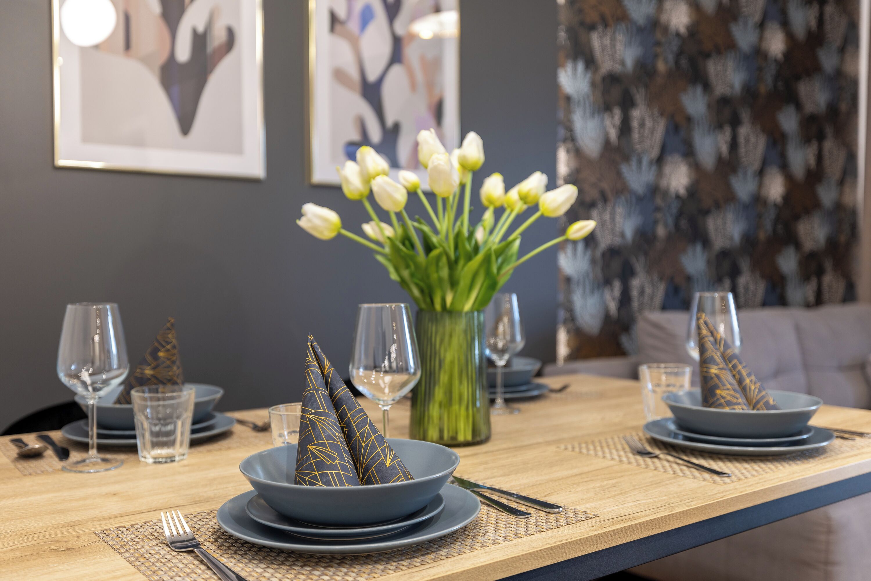 Et spisebord dækket med blå tallerkener, klare glas og en vase med hvide tulipaner.