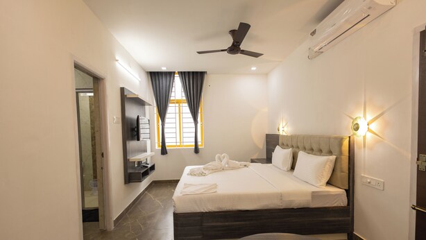 A modern hotel room with a large bed, a round table, a ceiling fan, and a TV mounted on the wall. - Hotel Kurunjii Residency (Yercaud)