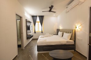 Een moderne hotelkamer met een groot bed, een ronde tafel, een plafondventilator en een aan de muur bevestigde televisie.