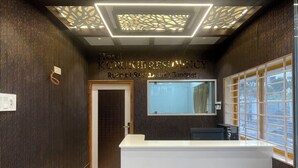 A reception area with a modern design, featuring a reception desk, a large mirror, and a patterned ceiling. - Hotel Kurunjii Residency (Yercaud)