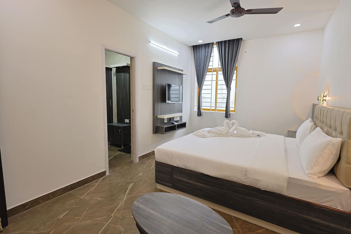 A modern hotel room with a large bed, a flat-screen TV mounted on the wall, a ceiling fan, and a bathroom visible through an open door.