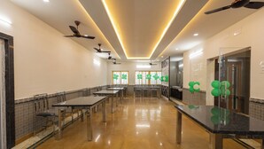 A spacious room with multiple tables and chairs, ceiling fans, and a glass partition with green balloons. - Hotel Kurunjii Residency (Yercaud)