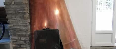 Una chimenea de piedra con una chimada de cobre, un muro de piedra y un banco rojo.