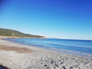 Una spiaggia con acqua cristallina, una riva sabbiosa e una collina con un edificio sullo sfondo.