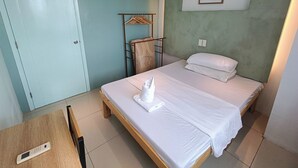 A bedroom with a single bed, a wooden bedside table, a wall-mounted shelf, and a door.