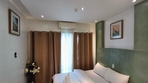 A hotel room with a bed, curtains, a vase with flowers, and two framed pictures on the walls.