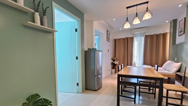 A modern kitchen with a refrigerator, a dining table with chairs, and a potted plant.