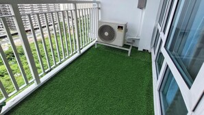 A balcony with artificial green turf, a white railing, and a window.