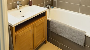 A bathroom with a white sink, wooden vanity, and a bathtub. - Charming apartment with terrace (Le Cannet)