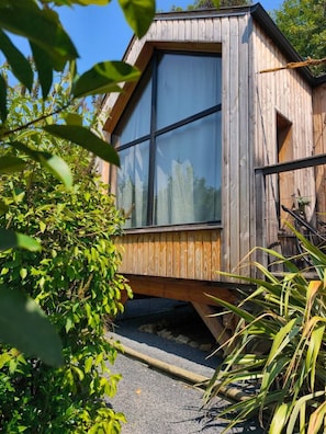 A wooden cabin with large windows, surrounded by greenery. - Lodge des Dentelles - Les Cabanes de Provence (Lafare)