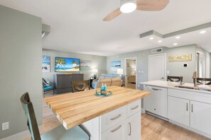 A modern kitchen with a wooden island, white cabinetry, and a ceiling fan.