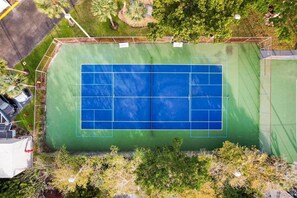 An aerial view of a tennis court with surrounding greenery and a building in the background.