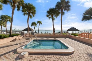 A swimming pool with lounge chairs and palm trees, overlooking a body of water. - The Riverside Club - B204 (Marco Island)