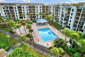A multi-story hotel with a central swimming pool surrounded by palm trees and lounge chairs.