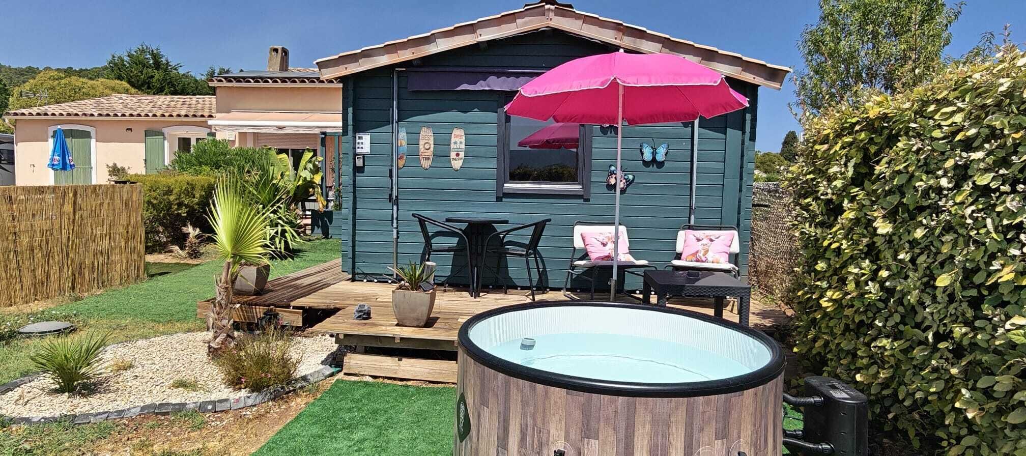 Une petite maison avec un jacuzzi, un espace salon extérieur et un jardin.