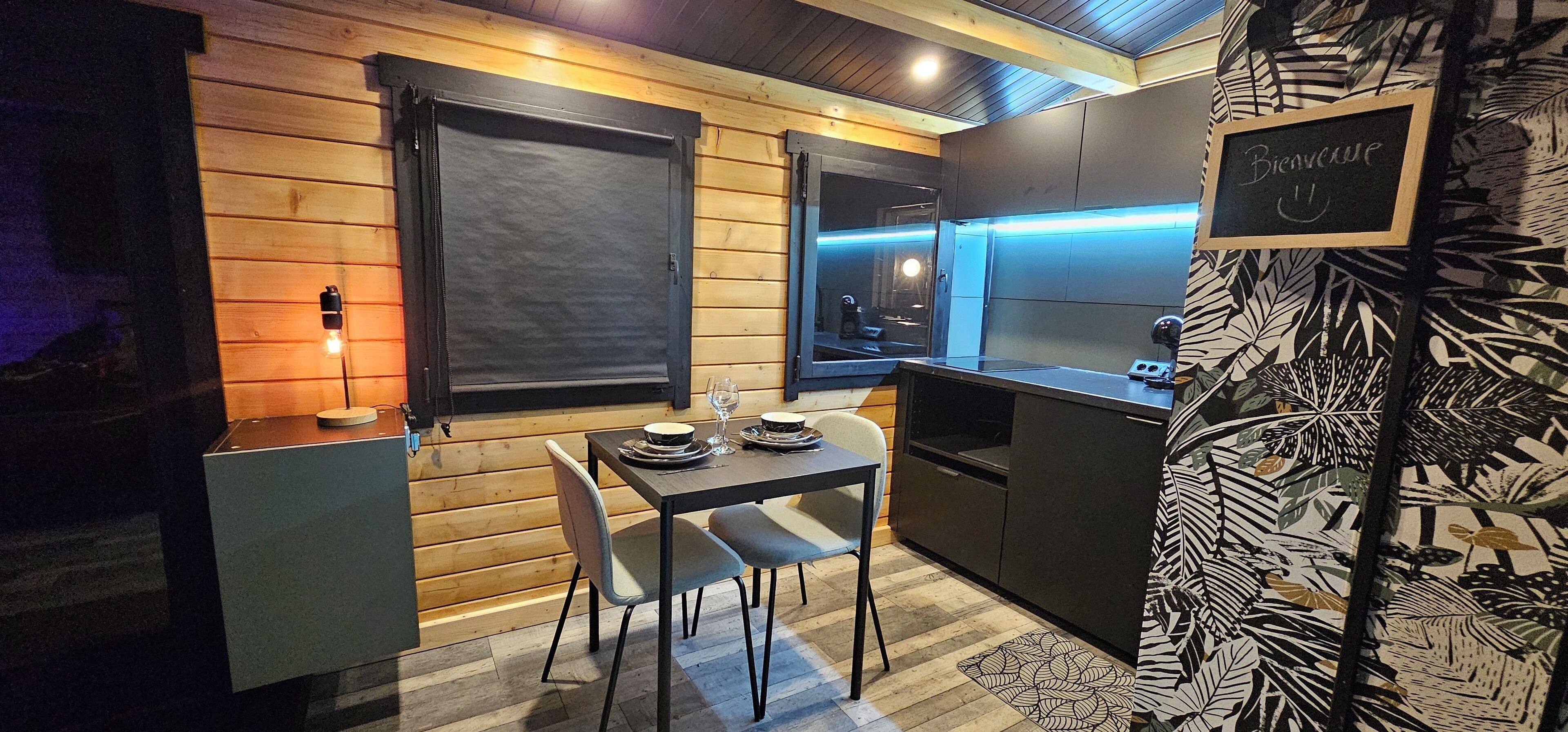 Een compacte keuken met houten wanden, een eettafel met stoelen en een kleine koelkast.
