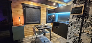 Una cocina compacta con paredes de madera, una mesa de comedor con sillas y un refrigerador pequeño.
