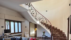 Uma ampla sala de estar com uma escada curva, um sofá modular e piso de mármore.