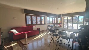 Um quarto espaçoso com um sofá vermelho, uma mesa de jantar com cadeiras e grandes janelas com vista para o exterior.