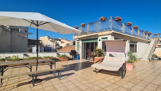 Terraço no telhado com área de estar coberta, plantas em vasos e escada que leva a um andar superior.
