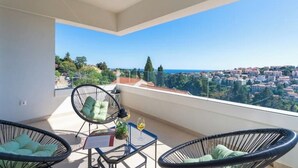 Ein Balkon mit Korbstühlen und einem Tisch, mit Blick auf eine Küstenstadt.