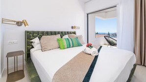 Ein Hotelzimmer mit großem Bett, Blick auf die Stadt, kleinem Tisch und Stuhl.