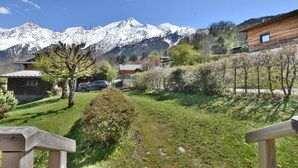 A mountain view with a wooden deck, a small garden, and a building with a sloped roof. - Authentic chalet at the foot of the Mont Blanc range (Les Houches)
