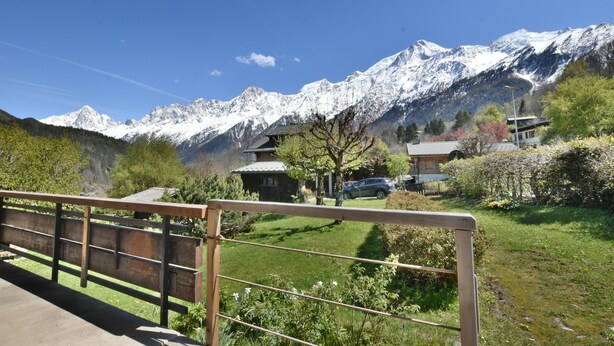 A mountain view with snow-capped peaks, a wooden fence, and a building with a sloped roof. - Authentic chalet at the foot of the Mont Blanc range (Les Houches)