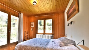 A wooden-paneled bedroom with a bed, a radiator, and a window with a view of greenery. - Authentic chalet at the foot of the Mont Blanc range (Les Houches)