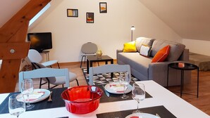 Un coin repas avec une table dressée pour deux personnes, un bol rouge et un téléviseur en arrière-plan.