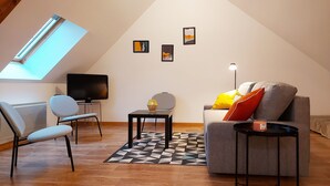 Un salon de style industriel, avec un plafond en pente, un téléviseur, un canapé, un fauteuil, une petite table et un lampadaire.