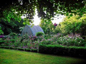 Une serre entourée de jardins luxuriants, où poussent différentes espèces de plantes à fleurs.