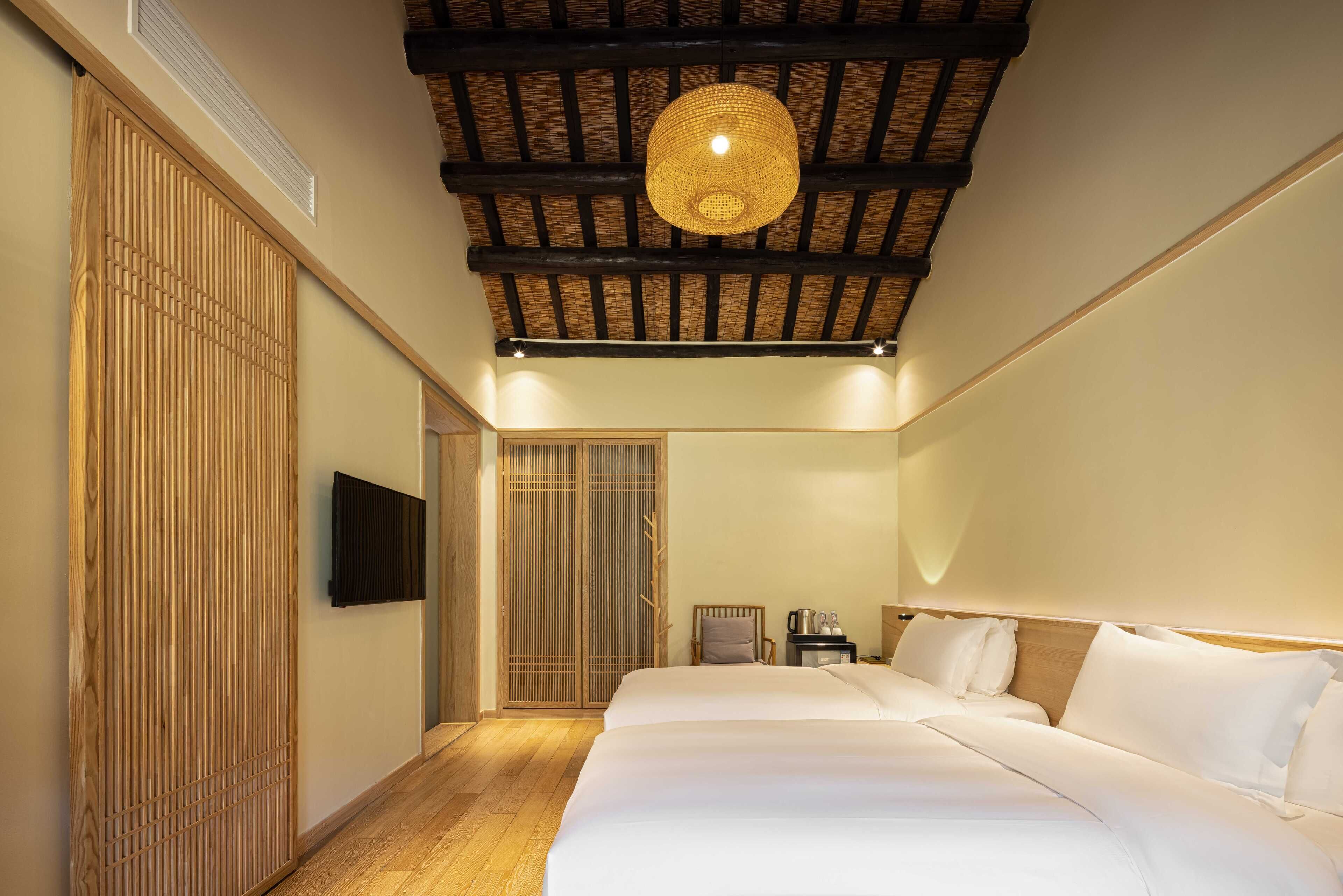 Een hotelkamer met een groot bed, een houten garderobe, een televisie en een plafond met zichtbare balken.
