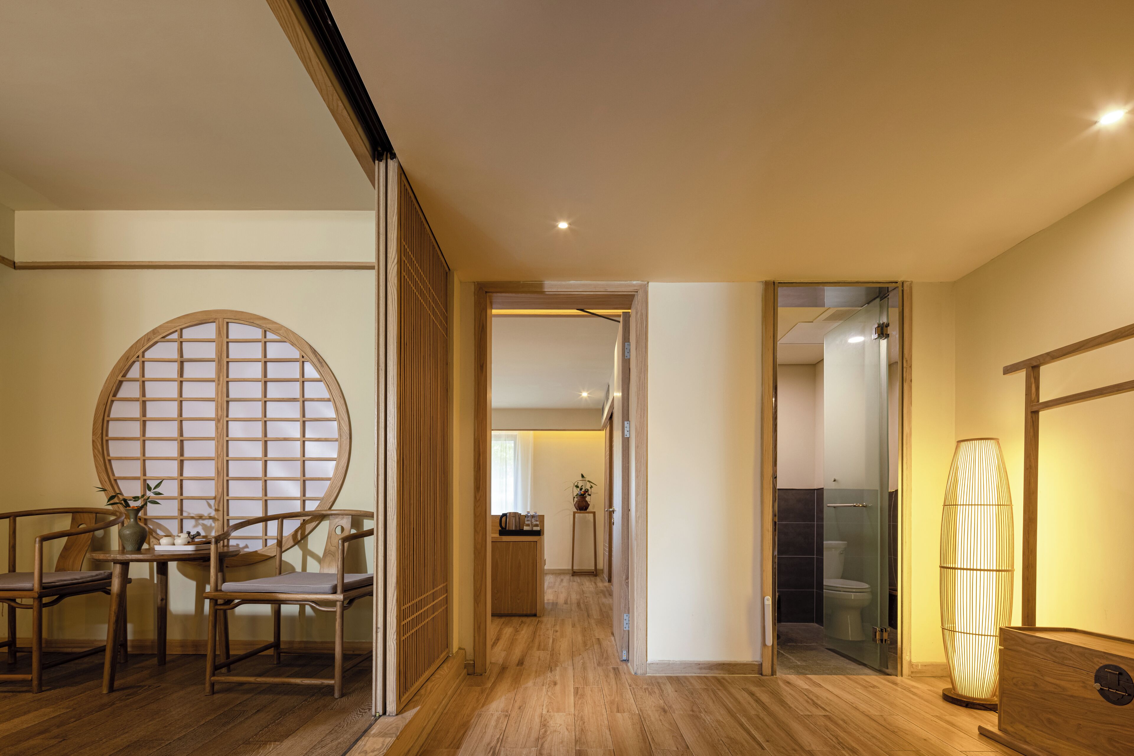 Un pasillo con suelo de madera, una mesa redonda de madera con sillas, un biombo japonés tradicional y una lámpara de pie alta.