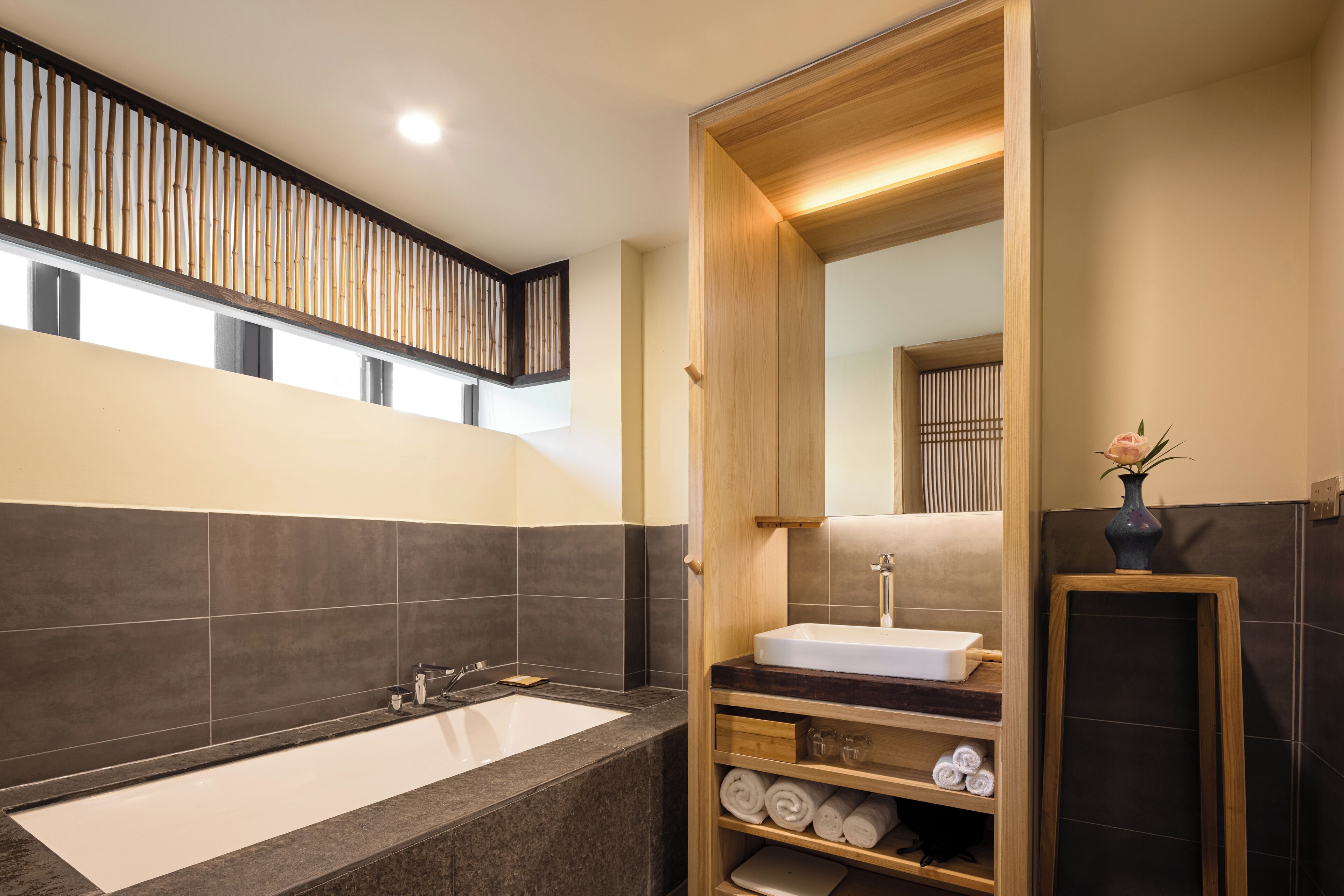 Un baño moderno con una bañera grande, estantes de madera con toallas y un espejo.