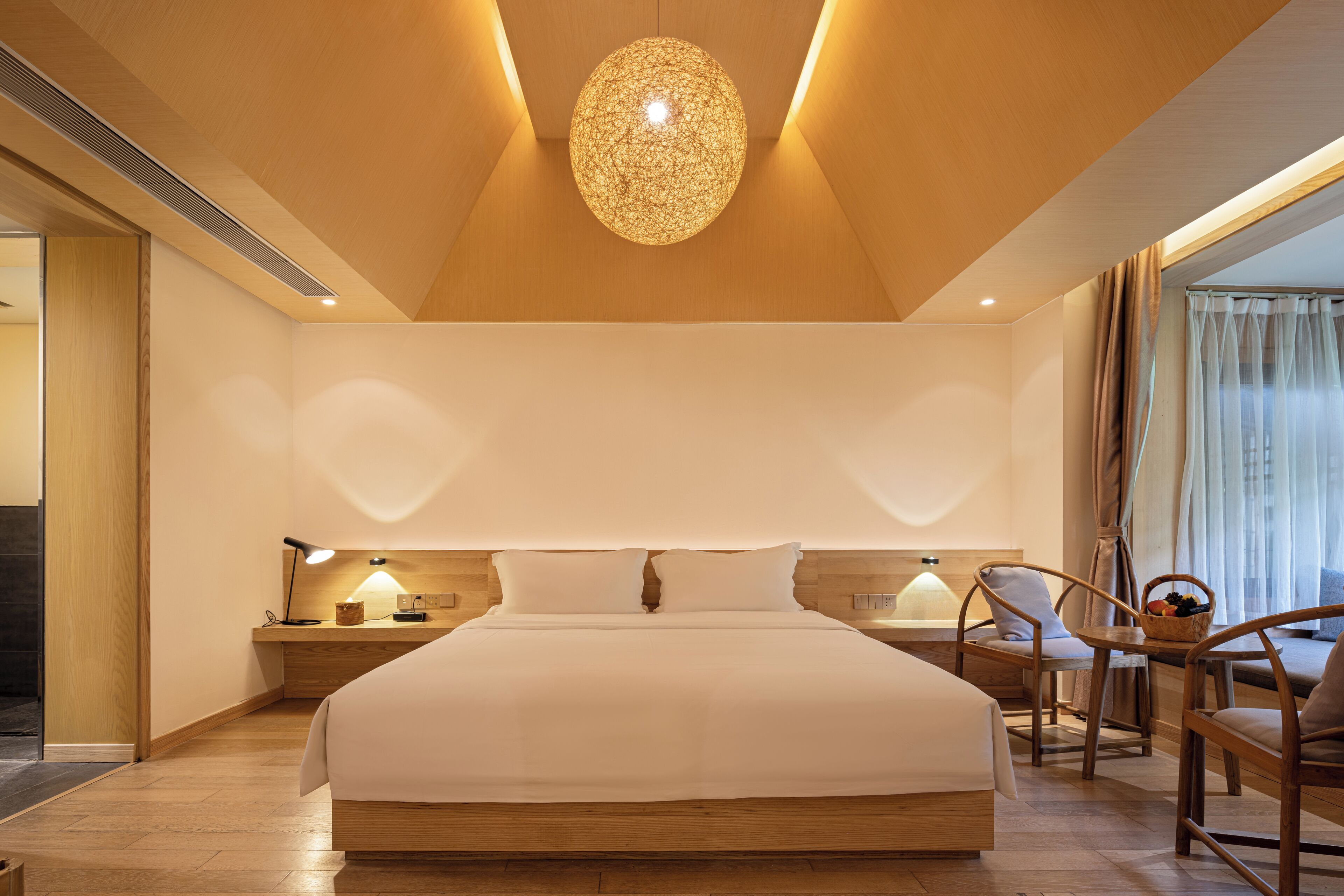Une chambre d’hôtel moderne dotée d’un grand lit, d’un plancher en bois, d ’un luminaire sphérique original et offrant une vue sur l’extérieur.
