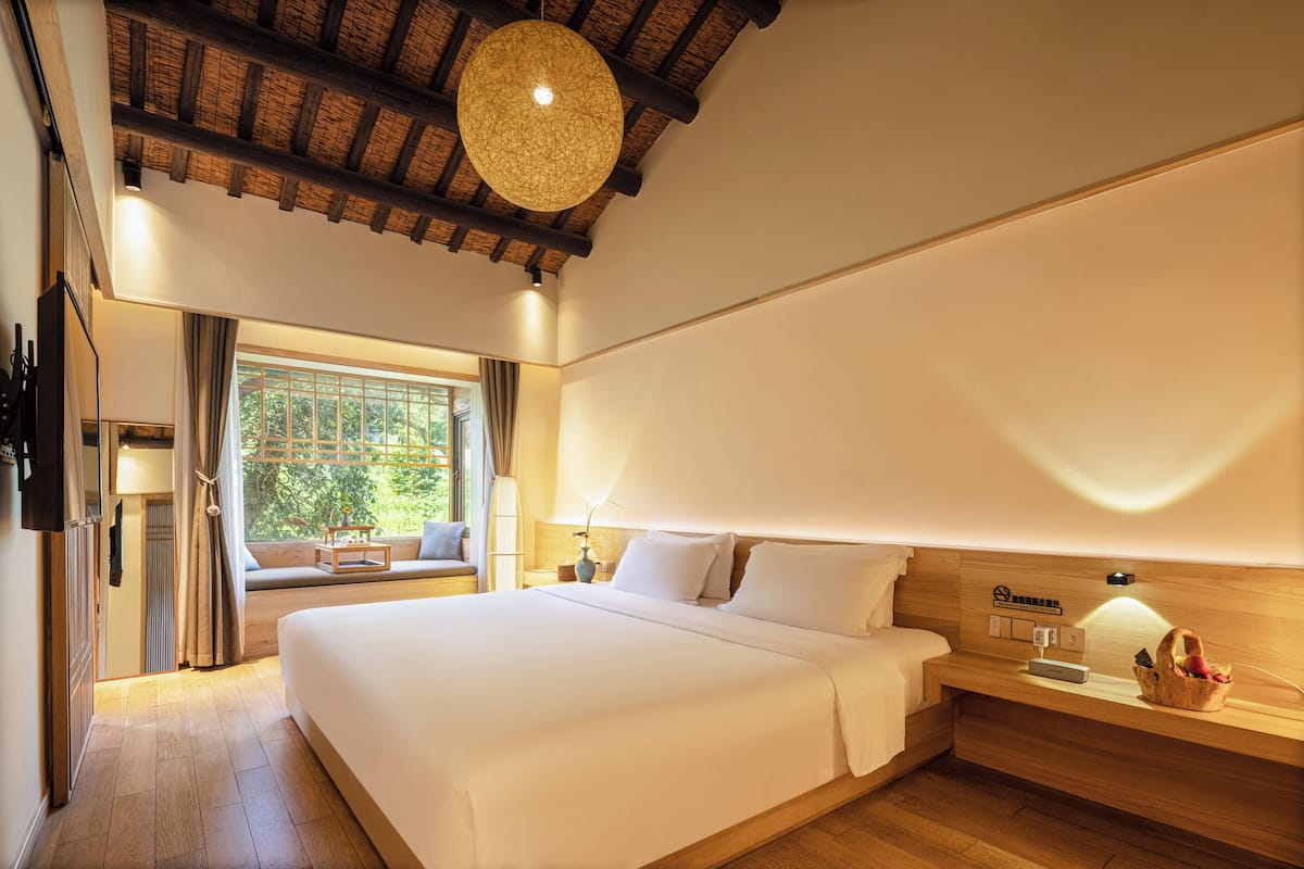 A spacious bedroom with a large bed, wooden headboard, bedside table, and a window with curtains.