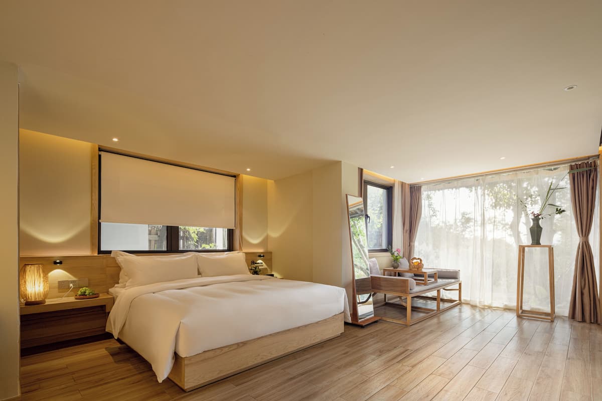 A modern bedroom with a large bed, bedside tables, a desk, and a window with curtains.