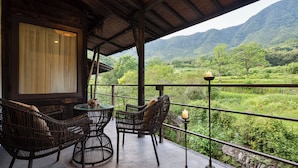 A balcony with wicker furniture, a candle, and a view of a lush green landscape with mountains in the background. - Tachuan Resort (Huangshan)
