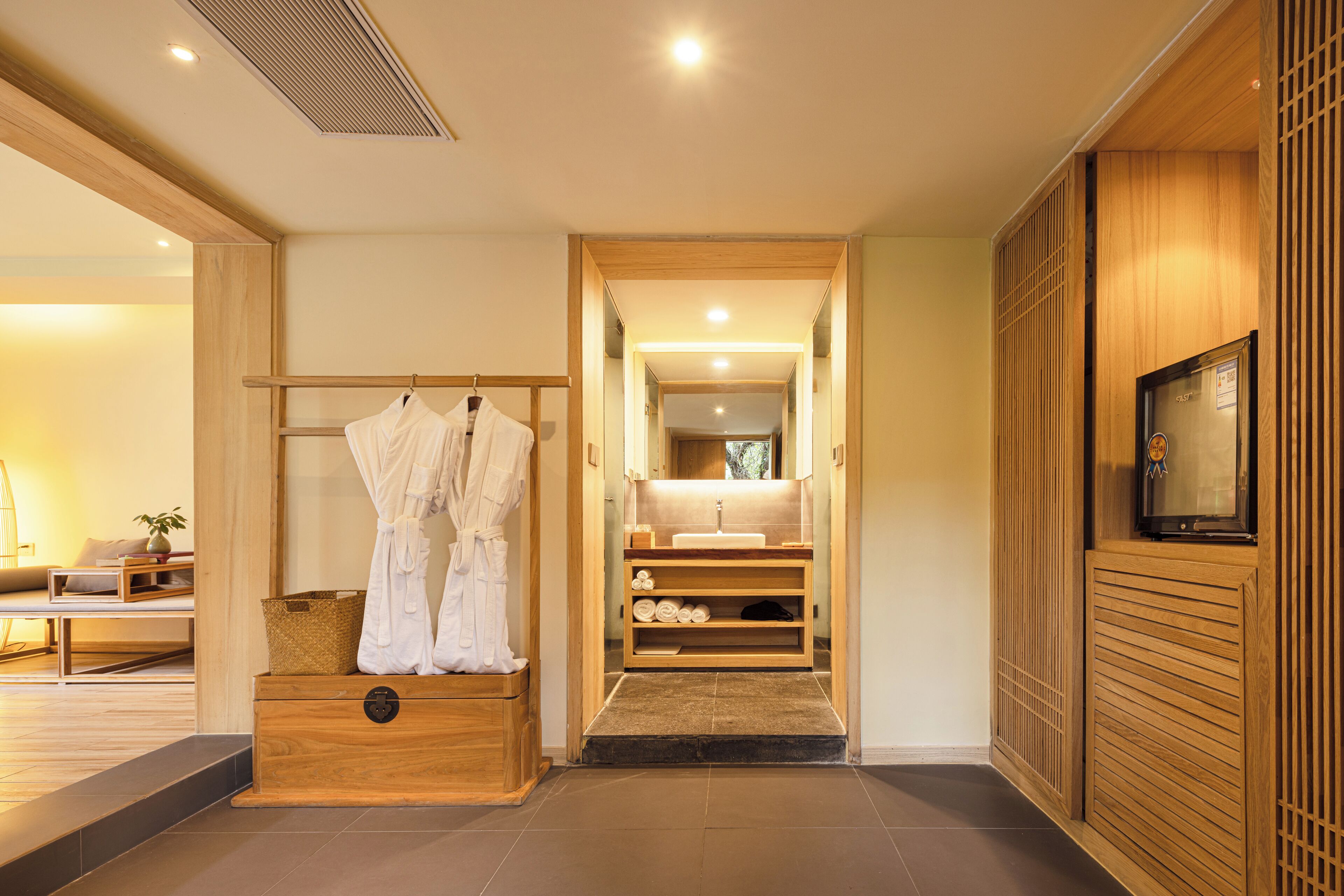 A modern bathroom with a wooden vanity, a robe rack, and a television on the wall.