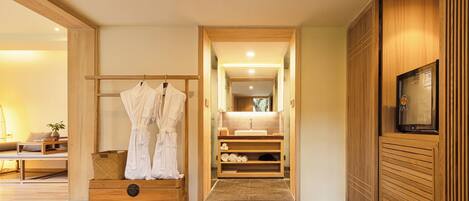 A modern bathroom with a wooden vanity, a robe rack, and a television on the wall.