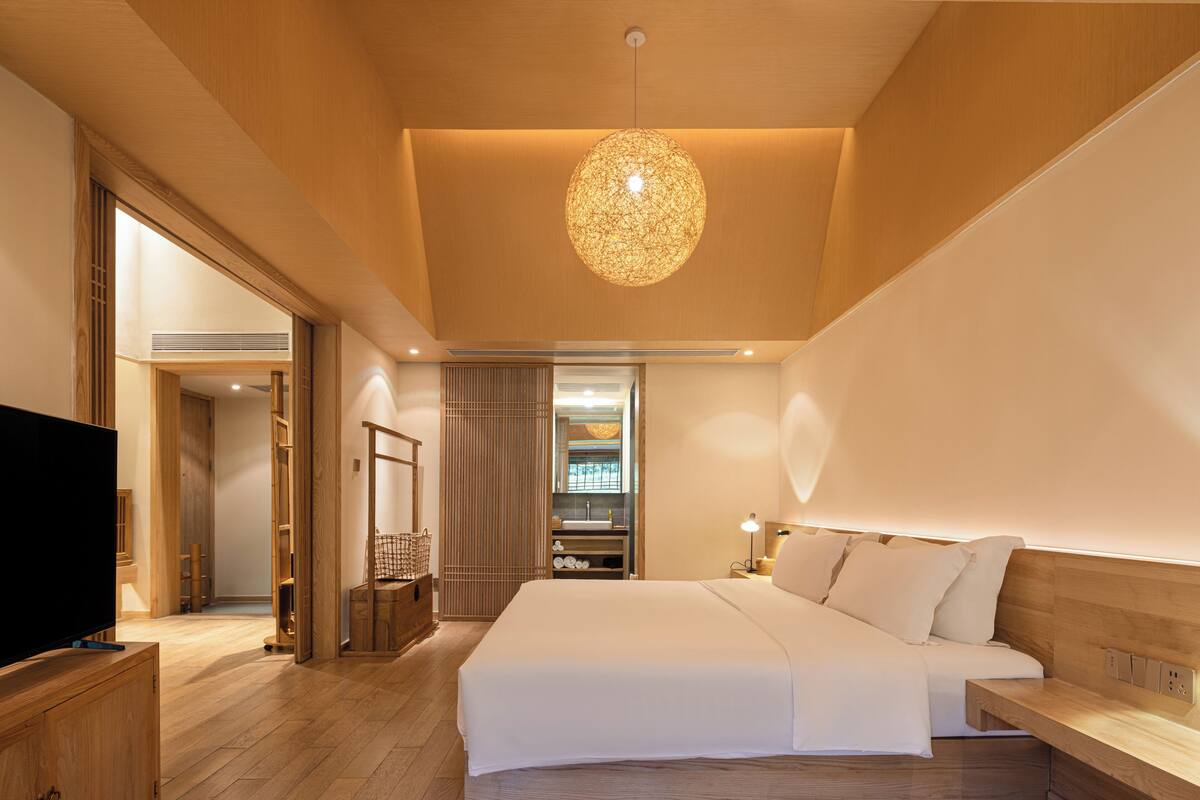 A modern hotel room with a large bed, wooden flooring, a television, and a unique spherical light fixture.
