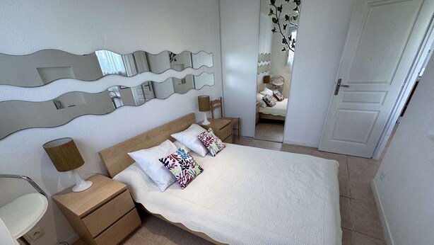 A neatly arranged bedroom with a bed, bedside tables, a lamp, and a mirror on the wall.