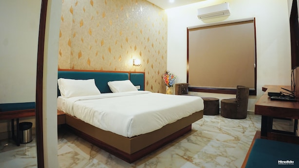 A hotel room with a large bed, a nightstand, a desk, and a chair. -  The Krati Resort (Bareilly)